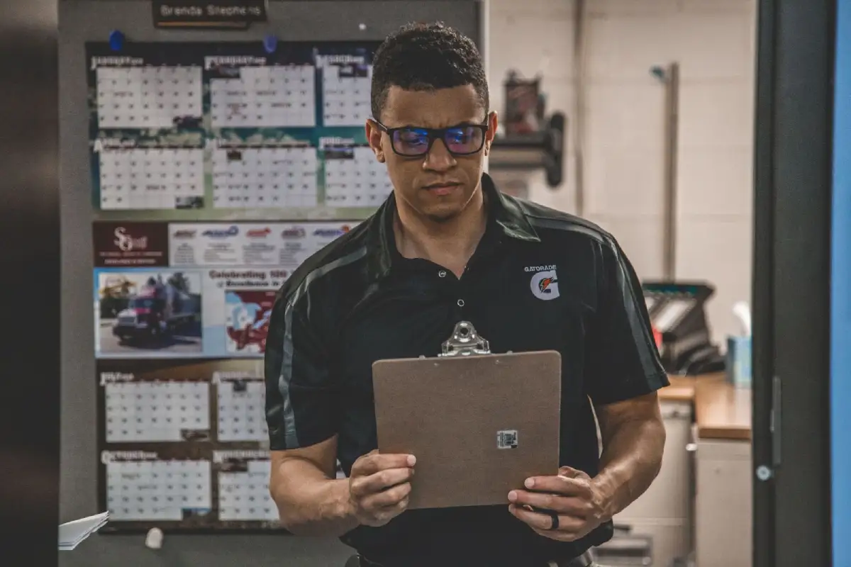 A supervisor reviews a maintenance checklist against a wall calendar to plan equipment servicing and ensure operational safety.