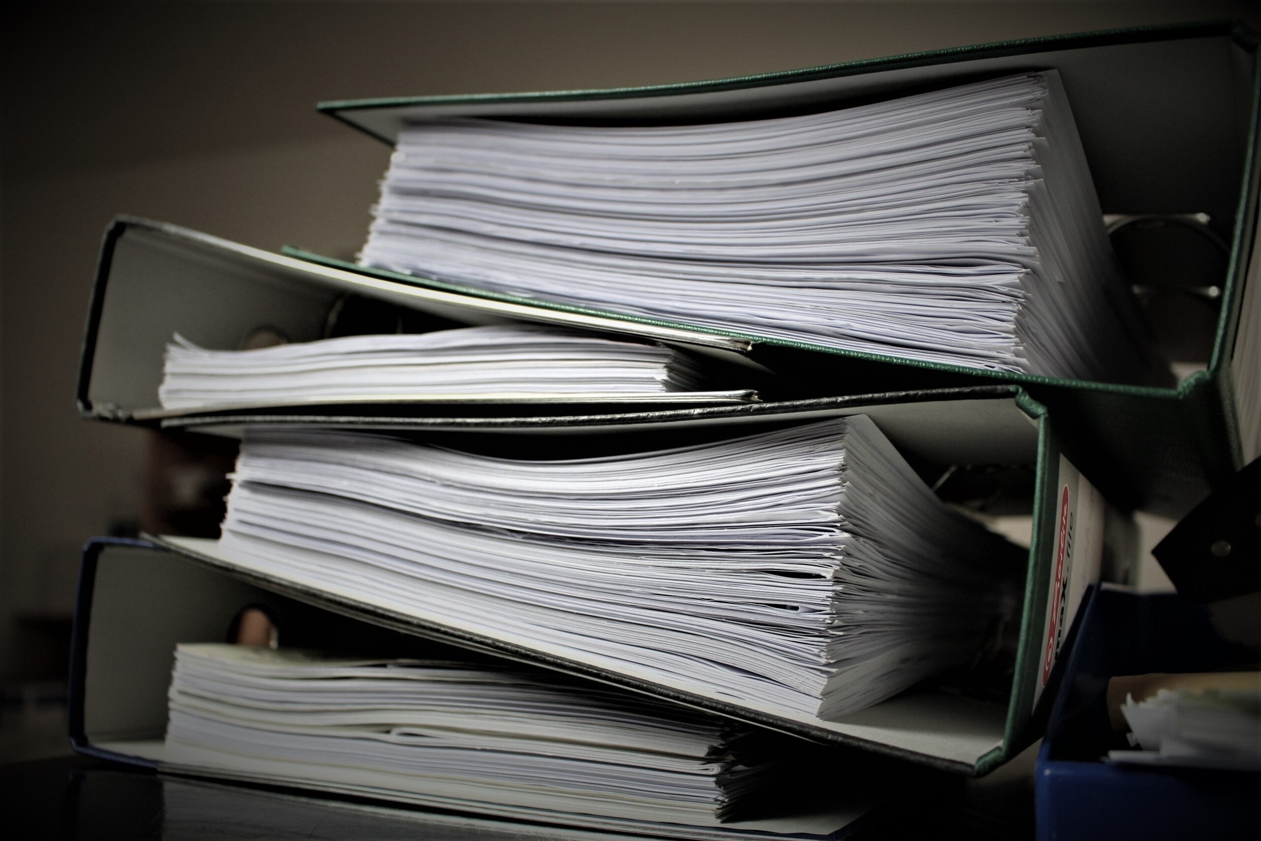 A close-up picture of four 3-ring binders filled with paper and all stacked on top of each other