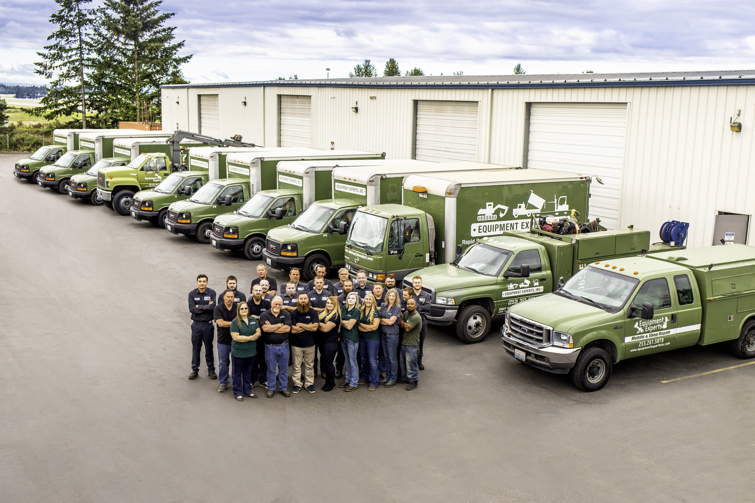An aerial drone-style picture of the Equipment Experts, Inc. team with their arms crossed and in front of their fleet of trucks