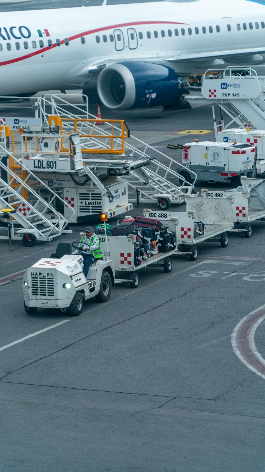 A class-VI forklift on an airplane tarmac tugging luggage away from an airplane