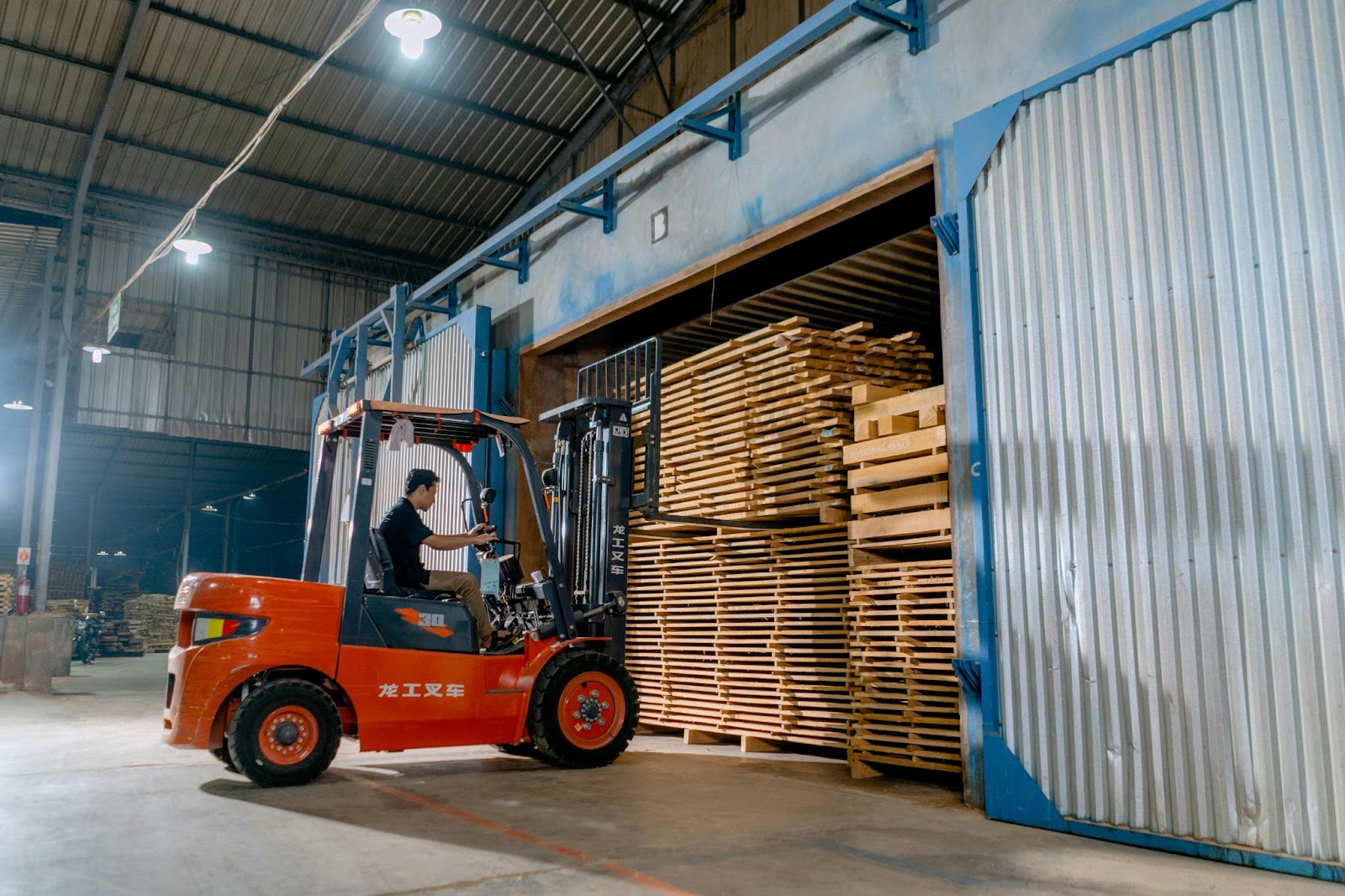 A person stabilizing a stack of wood pallets on forklift forks