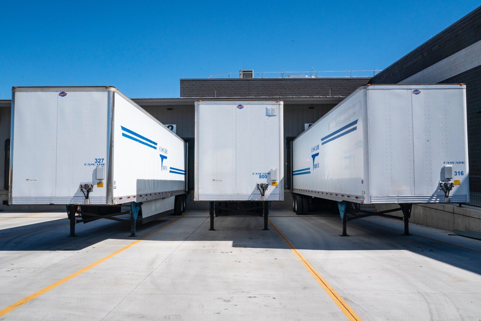 Three white box trailers parked at a loading dock outside a warehouse