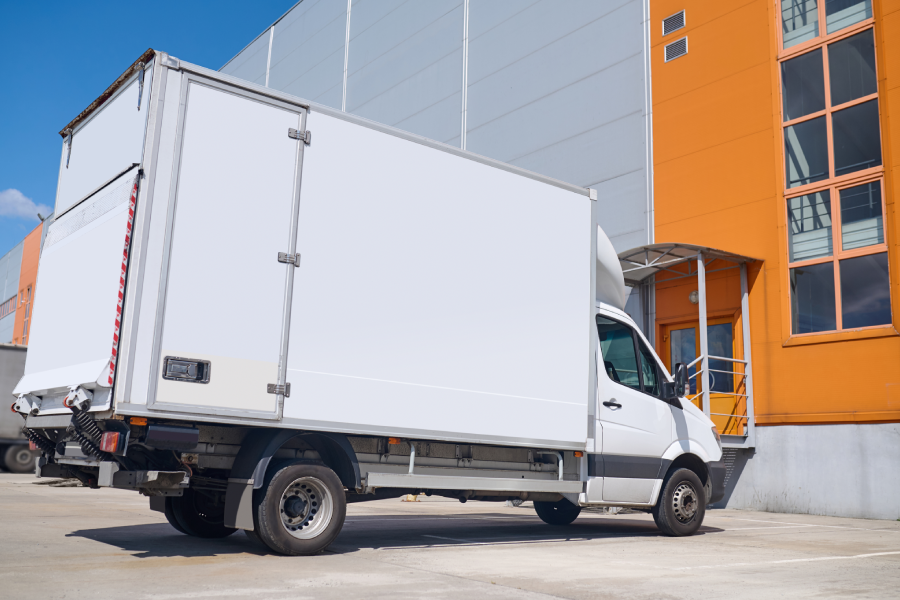 A white box truck parked outside a large commercial building.