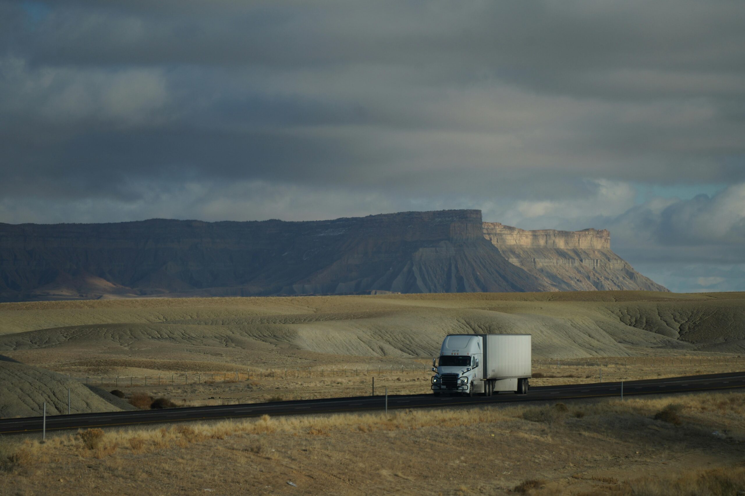 A semi truck on a lone road with mountains in the background