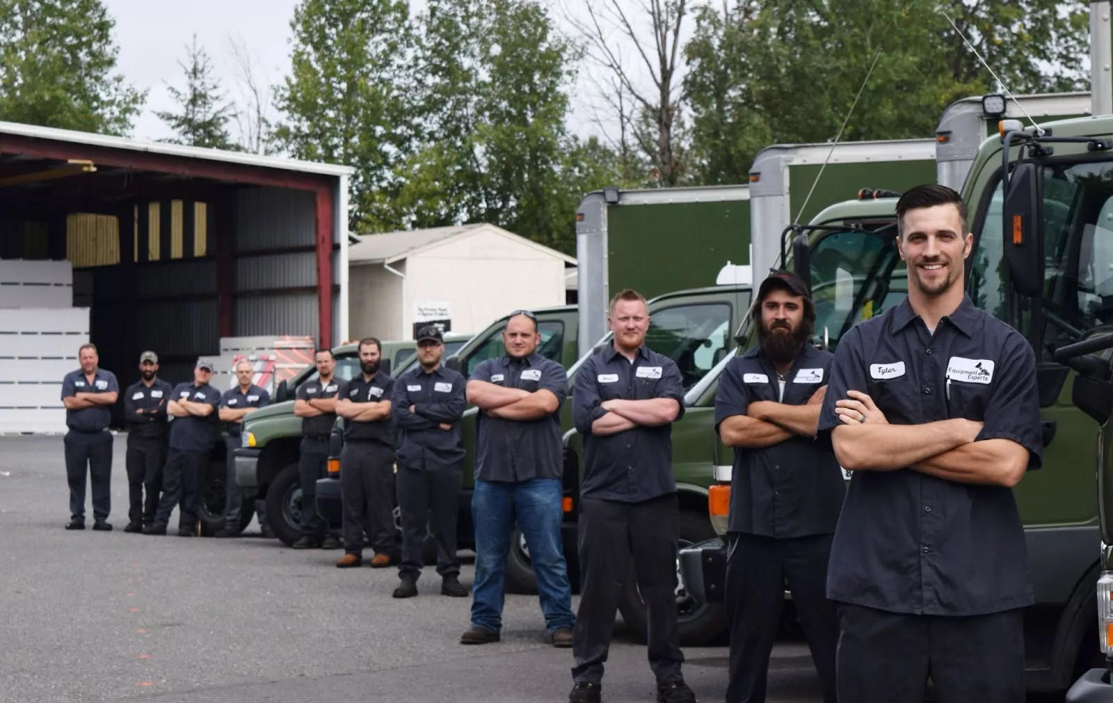 Diagonal view of men with crossed arms standing in front of trucks