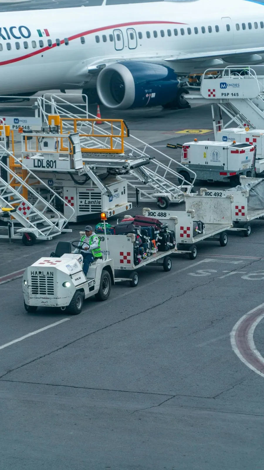 A class-VI forklift on an airplane tarmac tugging luggage away from an airplane