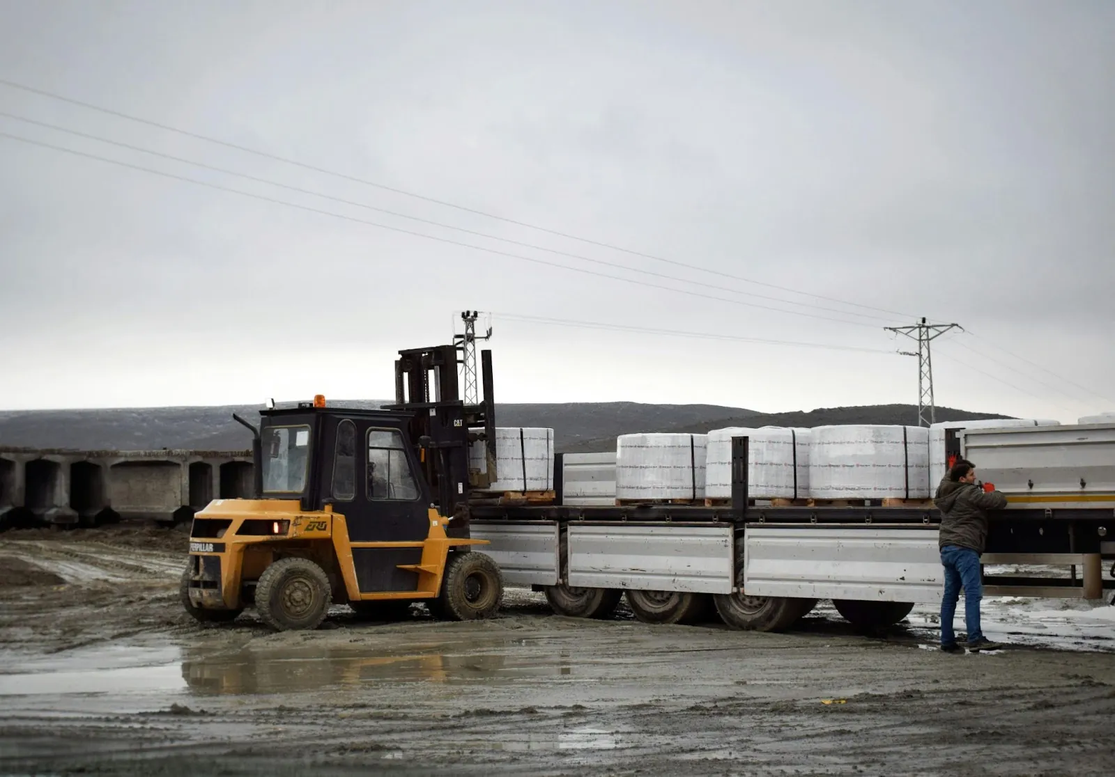 A forklift picking up a load from the top of a semi-truck flat bed trailer