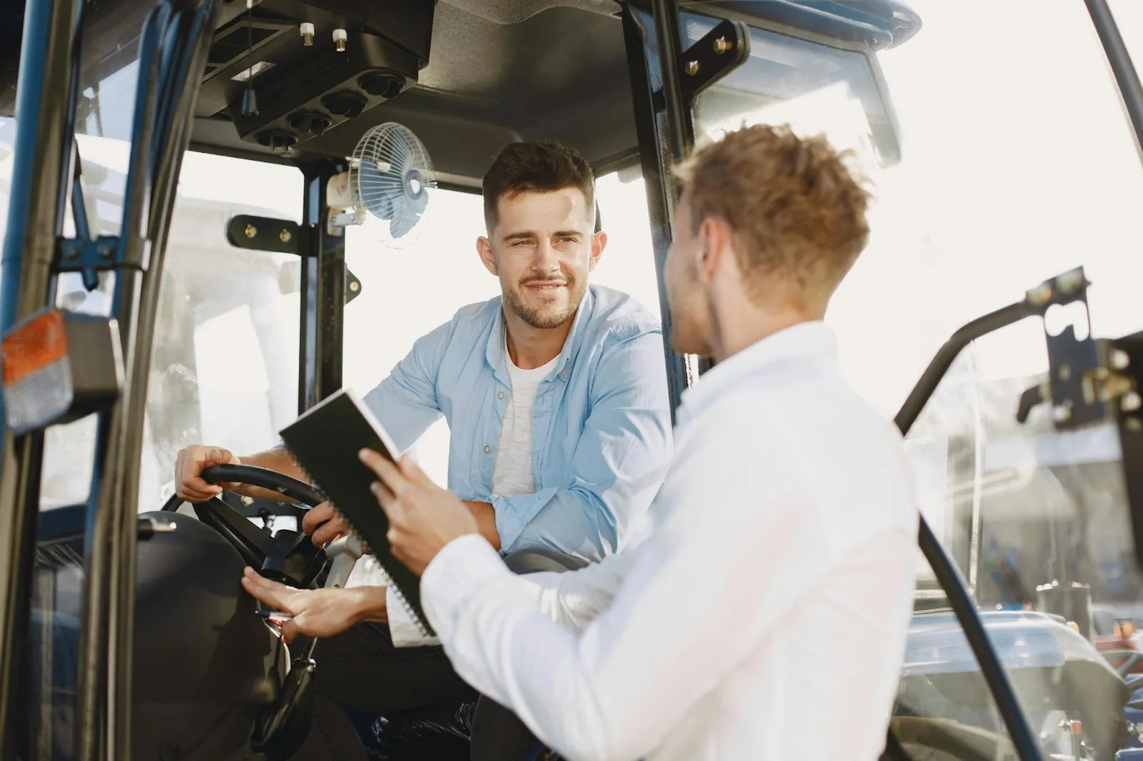 A gentleman in the seat of a forklift talking to a person outside the forklift